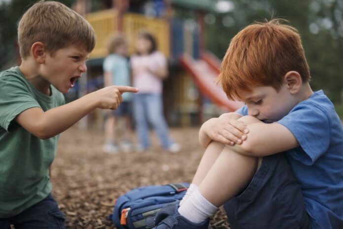 Anaokulunda zorbalık belirtileri: oyun alanında arkadaşının sözlü zorbalığına maruz kalan üzgün çocuk